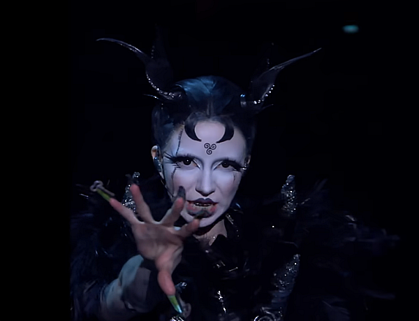 Bambie Thug Bambie Thug with antlers and dark makeup, gesturing in the half-light with her long fingernails.