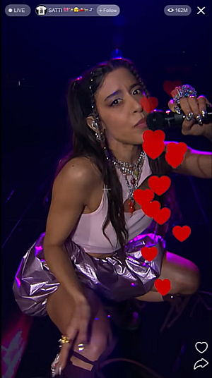 Marina Satti Marina Satti is crouched, wearing silver puffball breeches and a vest. Her nails are shimmering talons; there are rings on her fingers and there's a chain through her hair. Heart emojis rise up the portrait screen of a social media video.